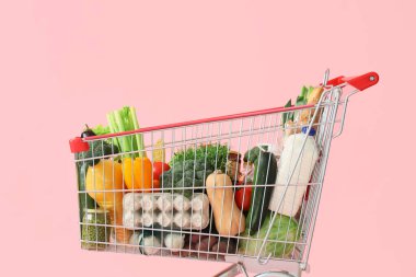 Pembe arka planda farklı taze ürünleri olan alışveriş arabası.