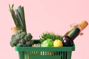 Pembe arka planda farklı taze ürünlerle yeşil alışveriş sepeti.