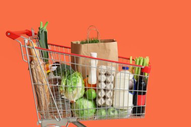 Turuncu arka planda farklı taze ürünleri olan alışveriş arabası.