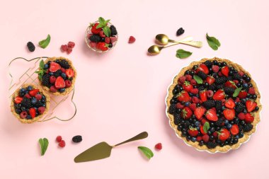 Tatlı tart ve tartlardan yapılmış çerçeve pembe arka planda farklı taze böğürtlenlerle