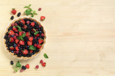 Farklı taze böğürtlenli tatlı tart ve ahşap zemin üzerinde nane.