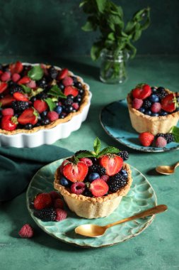 Sweet tartlets and tart with different fresh berries on green background