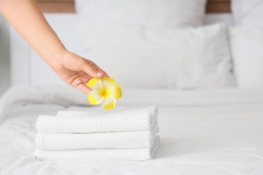 Female hand with clean towels and yellow plumeria flower on bed in hotel room, closeup