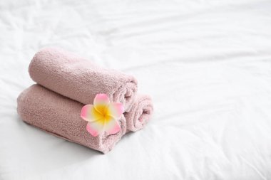 Otel odasındaki yatağın üzerinde pembe tesisat çiçeğiyle sarılmış temiz havlular.