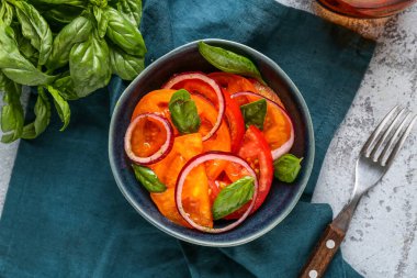 Gri arka planda kırmızı soğan ve fesleğen yapraklı taze domates salatası.