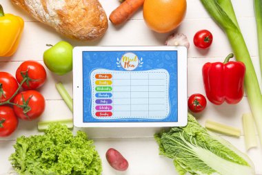 Yemek planlı tablet bilgisayar ve beyaz ahşap arka planda sağlıklı yiyecek.