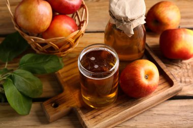 Şişe ve bir bardak taze elma şarabı, ahşap arka planda meyveler, yakın plan.