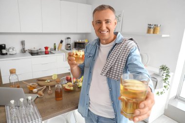 Mature man with glasses of apple cider in kitchen