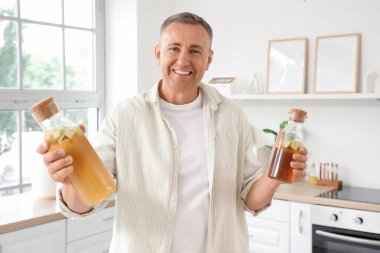 Mature man with bottles of apple cider in kitchen