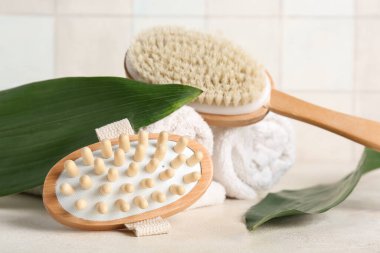 Beyaz masadaki yeşil yapraklar ve havlularla vücut masajı fırçaları.