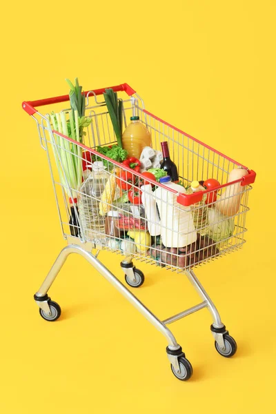 Sarı arka planda farklı taze ürünleri olan alışveriş arabası.