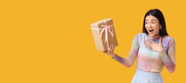 Sarı arka planda hediye kutusu olan şaşırmış genç bir kadın.
