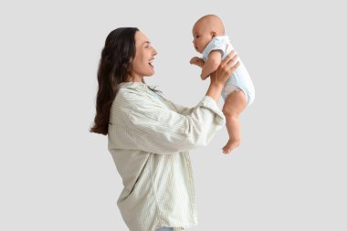 Beautiful young happy mother having fun with her cute little baby on grey background