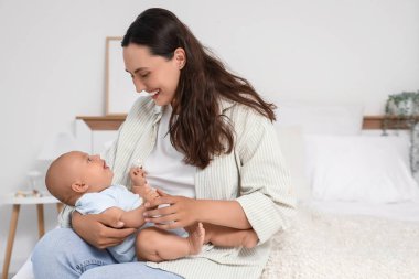 Beautiful young happy mother with her cute little baby sitting on bed at home
