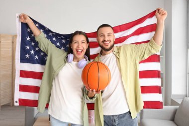 Young couple with ball and USA flag watching sport game at home