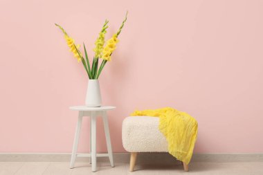 Güzel sarı gladiolus çiçekli vazo ve pembe duvarın yanındaki masada yumuşak puf.