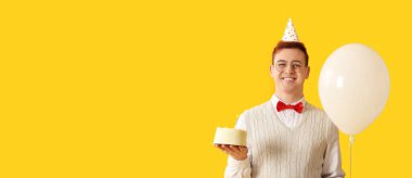 Happy young man in party hat holding balloon and sweet Birthday cake on yellow background with space for text