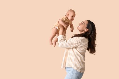 Beautiful young happy mother having fun with her cute little baby on beige background