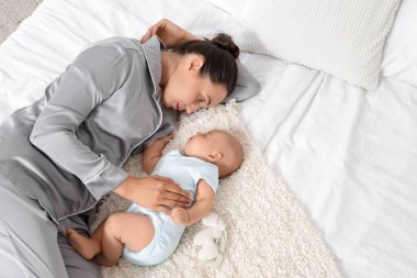 Happy young mother lying with her cute little sleeping baby on bed at home, top view