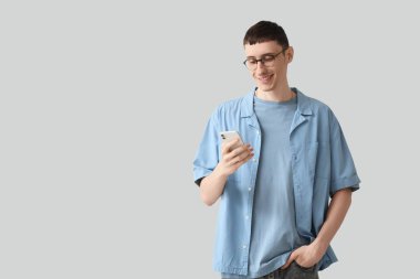 Young man in eyeglasses using mobile phone on white background