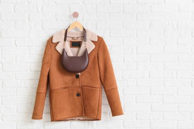 Koyun derisi ceket ve beyaz tuğla duvara asılı çanta.