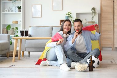İspanya bayrağı taşıyan genç çift evde futbol seyrediyor.