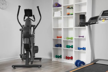 Interior of gym with elliptical machine, shelf unit and sports equipment