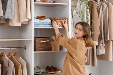 Young woman taking wicker organizer from shelf in wardrobe, back view