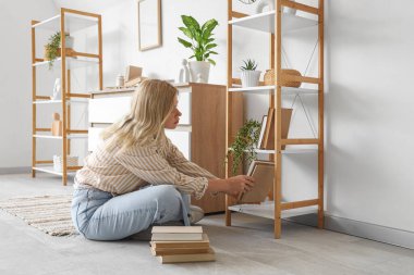 Young female interior designer putting books on shelving unit at home