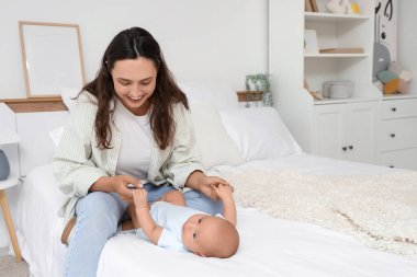 Beautiful young happy mother with her cute little baby sitting on bed at home