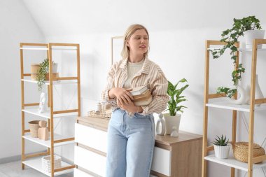 Beautiful young happy female interior designer with books decorating room at home