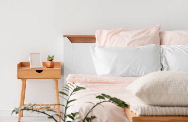 Bed with stylish pink bedding, bedside table and houseplant in bedroom