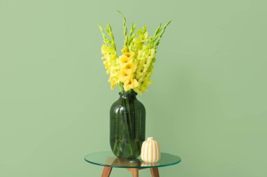 Yeşil arka planda güzel sarı gladiolus çiçekleri olan vazo.