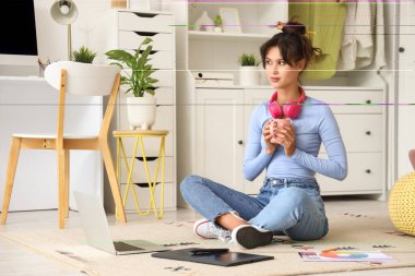 Female graphic designer with coffee cup sitting on carpet at home