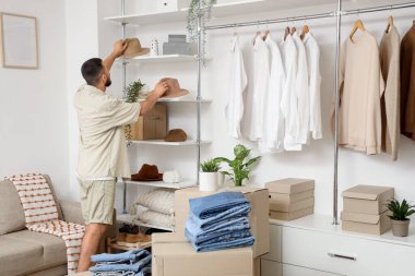 Young man putting hats on shelves in wardrobe, back view