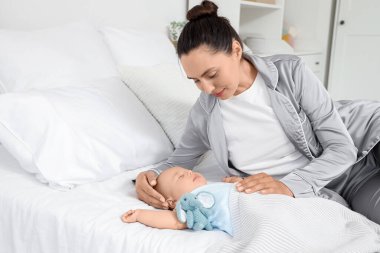 Happy young mother lying with her cute little sleeping baby and toy elephant on bed at home