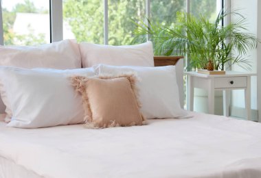 Şık pembe yataklı yatak, komodinli masa ve yatak odasının penceresinin yanındaki çiçek.