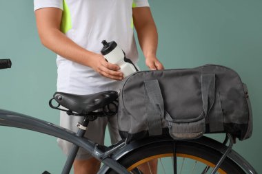 Man taking bottle of water from sports bag on bicycle against green background