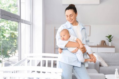 Beautiful young happy mother with her cute little baby near window at home