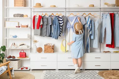 Young woman with hanging clothes in wardrobe, back view