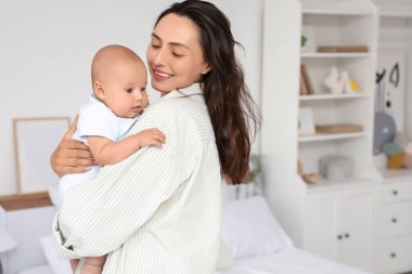 Beautiful young happy mother with her cute little baby in bedroom at home