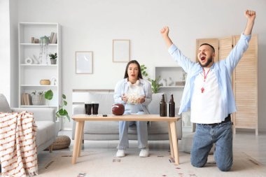 Young couple with popcorn watching rugby game at home