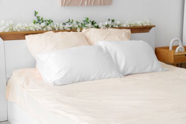 Bed with stylish pink bedding, flowers and bedside table in bedroom