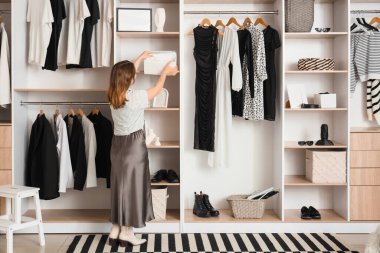 Young woman taking organizer from shelf in wardrobe, back view