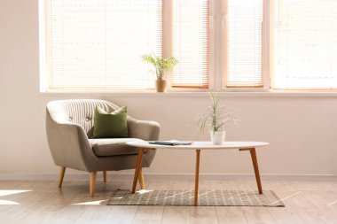 Oturma odasının içinde, koltuğu, çiçekleri ve dergileri pencere kenarındaki sehpanın üzerinde.