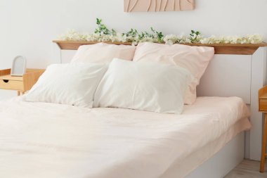 Bed with stylish pink bedding, flowers and bedside tables in bedroom