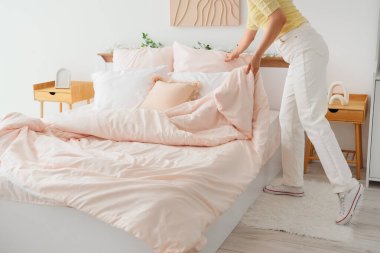 Young woman making bed with pink blanket at home, closeup