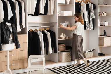 Young woman taking organizer from shelf in wardrobe