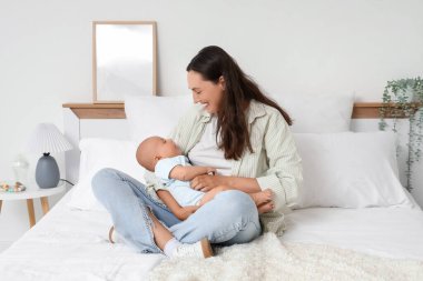 Beautiful young happy mother with her cute little baby sitting on bed at home
