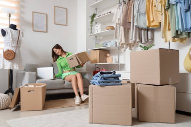 Young woman with wardrobe box using laptop on sofa in dressing room